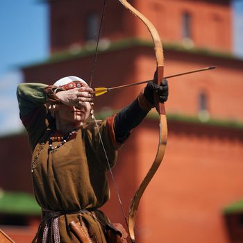 Medieval archery tournament. A woman shoots an arrow in the medieval castle yard. Woman in medieval dress with a wooden bow in her hands. historical reconstruction. 14.05,2022. Yoshkar-Ola, Russia.