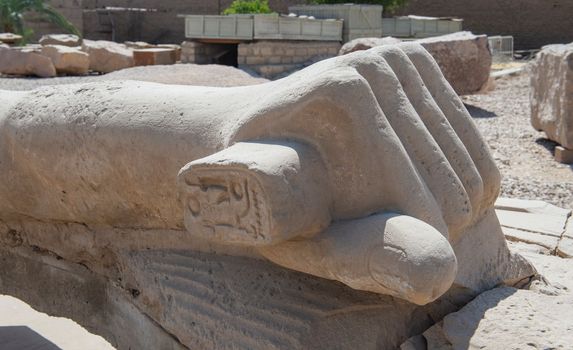 Large broken statue of Ramses II hand in ancient egyptian Karnak Temple laying down being restored