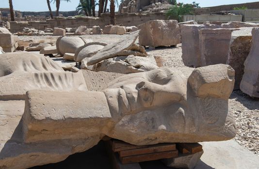 Large broken statue of Ramses II head in ancient egyptian Karnak Temple laying down being restored