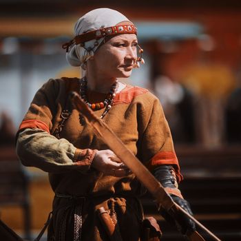 Medieval archery tournament. A woman shoots an arrow in the medieval castle yard. Woman in medieval dress with a wooden bow in her hands. historical reconstruction. 14.05,2022. Yoshkar-Ola, Russia.