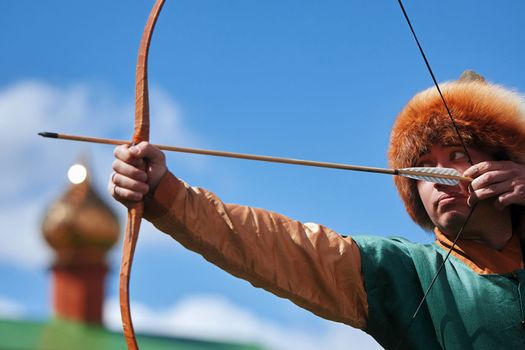 Medieval archery tournament. Man shoots an arrow in the medieval castle yard. Man in medieval dress with a wooden bow in her hands. historical reconstruction. 14.05,2022. Yoshkar-Ola, Russia.