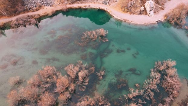 Turquoise blue mirror water with trees in the lake. Light streaks from underwater streams are visible. Autumn mountains and coniferous trees are reflected in the water. Issyk Mountain Lake, Kazakhstan