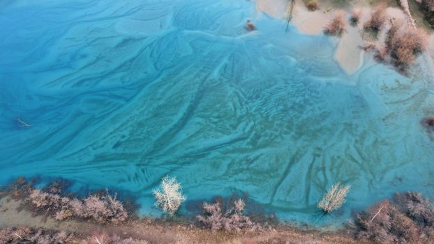 Turquoise blue mirror water with trees in the lake. Light streaks from underwater streams are visible. Autumn mountains and coniferous trees are reflected in the water. Issyk Mountain Lake, Kazakhstan