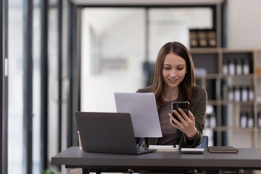 Business woman using smartphone for do math finance on wooden desk in office, tax, accounting, financial concept