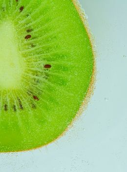 Close-up of kiwi fruit in liquid with bubbles. Slice of green ripe kiwi fruit in sparkling water. Juicy kiwi fruit in carbonated water. Macro vertical image.
