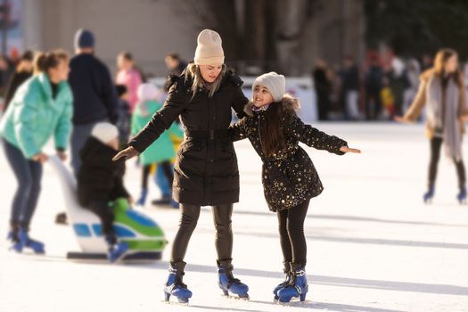 Action shot of beautiful woman teaching her daughter how to ice skate.