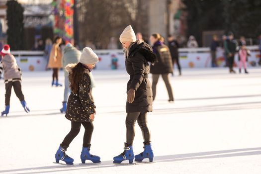 Action shot of beautiful woman teaching her daughter how to ice skate.