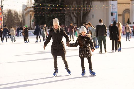 Action shot of beautiful woman teaching her daughter how to ice skate.