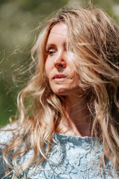 Portrait of a blonde in the park. Beautiful woman with long blond hair in a blue dress