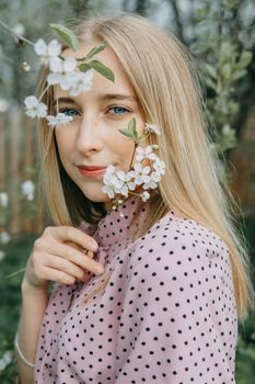 Blonde girl on a spring walk in the garden with cherry blossoms. Female portrait, close-up. A girl in a pink polka dot dress