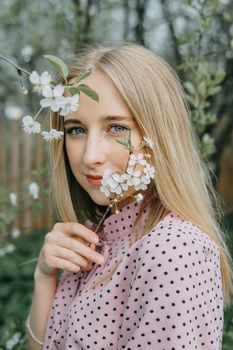 Blonde girl on a spring walk in the garden with cherry blossoms. Female portrait, close-up. A girl in a pink polka dot dress