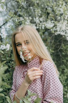 Blonde girl on a spring walk in the garden with cherry blossoms. Female portrait, close-up. A girl in a pink polka dot dress