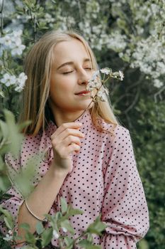 Blonde girl on a spring walk in the garden with cherry blossoms. Female portrait, close-up. A girl in a pink polka dot dress