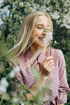 Blonde girl on a spring walk in the garden with cherry blossoms. Female portrait, close-up. A girl in a pink polka dot dress