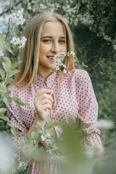 Blonde girl on a spring walk in the garden with cherry blossoms. Female portrait, close-up. A girl in a pink polka dot dress