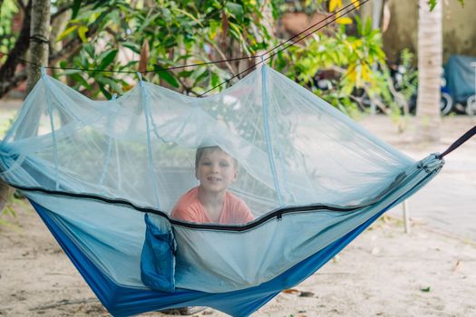 Smile child boy lie rest hammock with mosquito net. Happy childhood daydream. Look at from, laughing, portrait.