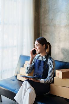 Starting small business entrepreneur of independent Asian female online seller talking on the phone with a customer and packing products for delivery to the customer. and SME delivery concept.