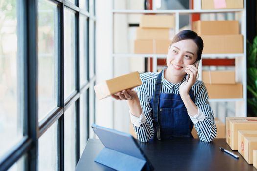 Starting small business entrepreneur of independent Asian female online seller talking on the phone with a customer and packing products for delivery to the customer. and SME delivery concept.