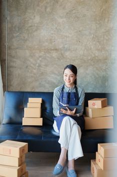 Starting small business entrepreneur of independent Asian female online seller talking on the phone with a customer and packing products for delivery to the customer. and SME delivery concept.