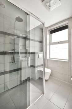 a modern bathroom with white and gray tiles on the walls, glass shower stall and toilet in the middle part of the room