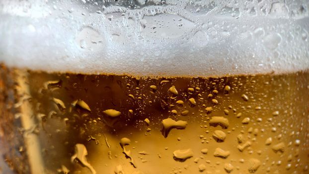 White foam and unfocused drops of water on a glass of chilled golden beer.Macrophotography.Selective focus.Texture or background