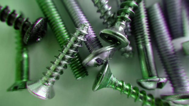 Screws bolts of different sizes randomly lie on the table and are highlighted in green . Macrophotography.Texture or background.Selective focus.