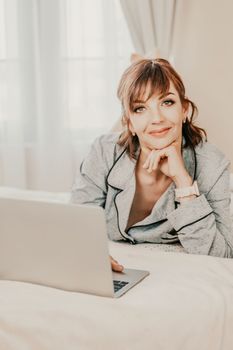 Freelancer woman wears pajamas, she lies in bed and uses work on laptop, computer, study on the Internet, surf the internet, relax, relax, spend time in the bedroom, living room, at home, in the hotel room, wake up