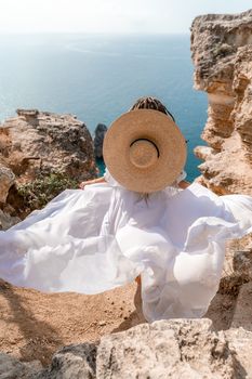 Woman white dress sea rocks. A girl in a hat and a long white dress descends the stairs between the yellow rocks overlooking the sea. The stone can be seen in the sea. Travel photograph