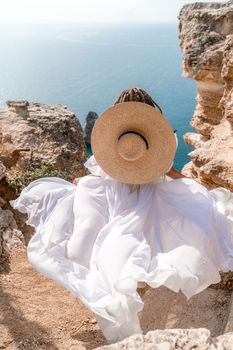 Woman white dress sea rocks. A girl in a hat and a long white dress descends the stairs between the yellow rocks overlooking the sea. The stone can be seen in the sea. Travel photograph