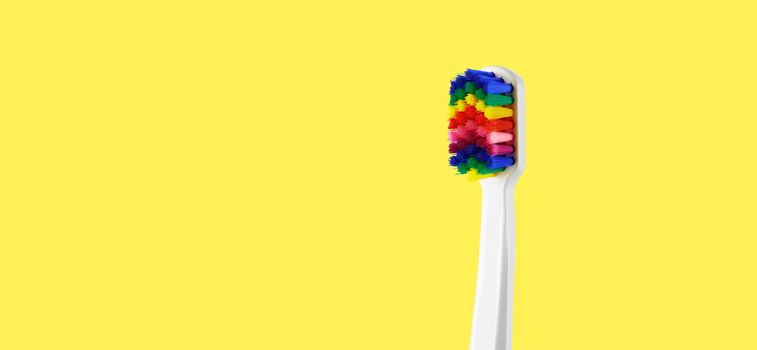 White toothbrush with multicolored bristles on yellow background. Bristles in all colors of the rainbow. Rainbow toothbrush with white knob. Fashionable oral care.