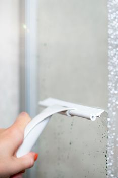 Shower cabin cleaning. Cleaning glass after using the shower. Cleaning glass with a rubber scraper