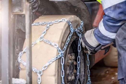 Close-up of male hands putting chains on a wheel. Examples of installing an anti-skid chain on a wheel in winter. Preparing a loader, tractor or truck for a snowy road.