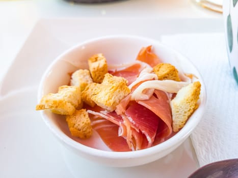 slices of jamon and croutons lie in a bowl for use in salad or soup.