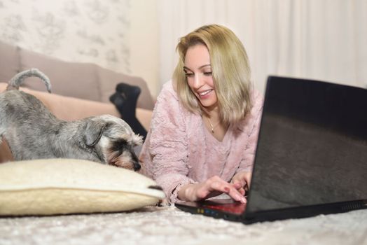 Dog lies on the carpet and asks for attention from a charming young lady who is working on a laptop at home