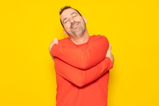 Bearded hispanic man completely excited and self-absorbed hugging himself showing he loves himself very much isolated over yellow background