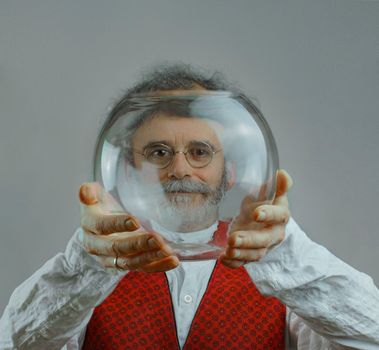 a colorful man with curls, a beard and a silver-colored mustache holds a transparent glass ball in his hands and looks through this ball. High quality photo