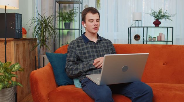 Portrait of blogger teen man sitting on couch, looking at camera, making video webcam conference call with friends or family, enjoying pleasant conversation. Young guy laughing, waving hello at home