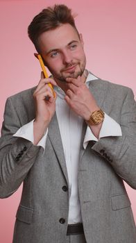 Happy bearded business man boss at office workspace making phone call conversation communication. Young freelancer guy boy enjoying mobile talking with colleague on pink studio background. Vertical