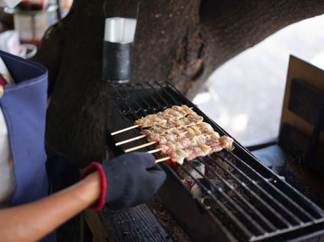 Hand holding grilled pork sticks on fire flaming in steel stove vintage style, delicious Thai street food and popular concept  .