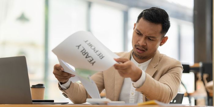 Stressed Asian businessman worry with many document on desk at office.