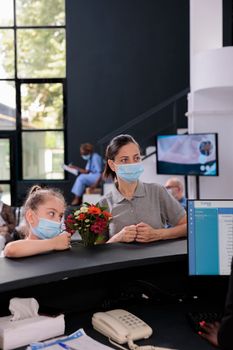 Receptionist talking with mother and child explaining medical expertise during checkup visit appointment in hospital reception. People wearing protective face mask to prevent infection with covid19