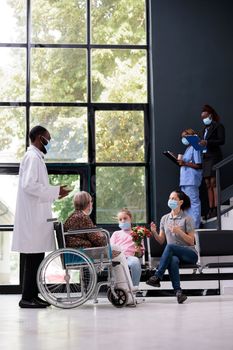 Doctor discussing medical expertise with patient daughter explaining health care treatment during consultation in hospital office. People wearing face mask to prevent infection with covid19