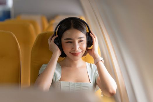 Joyful asian woman sits in the airplane and using tablet while go to travel.