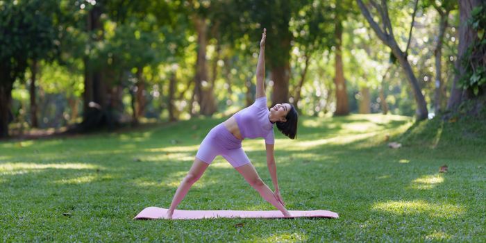 Attractive Asian female in sportswear practicing yoga in the outdoor park.