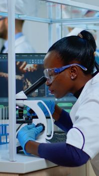 Black woman chemist analysing reaction of virus on microscope in laboratory. Multiethnic team examining vaccine evolution using high tech for scientific research, treatment development against covid19