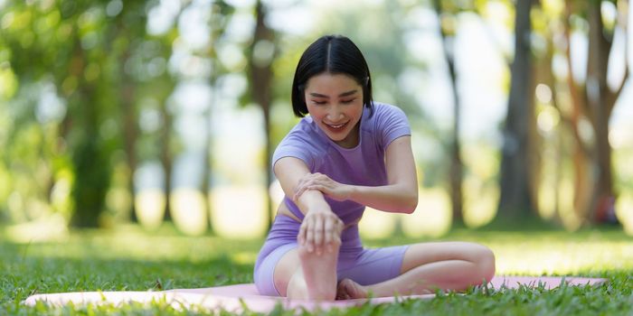 Attractive Asian female in sportswear practicing yoga in the outdoor park.