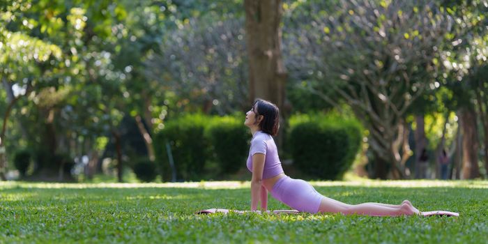 Attractive Asian female in sportswear practicing yoga in the outdoor park.