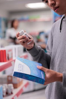 Male client examining sleeping pills box, looking at healthcare products and medication on pharmacy shelves. Young man buying sedatives and medical supplements or pharmaceutics. Close up.