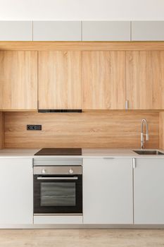 Closeup of piece of modular kitchen furniture made of light wood. Modern cozy kitchen interior with appliances built into marble countertop. Hood hidden from view in cabinet above stove