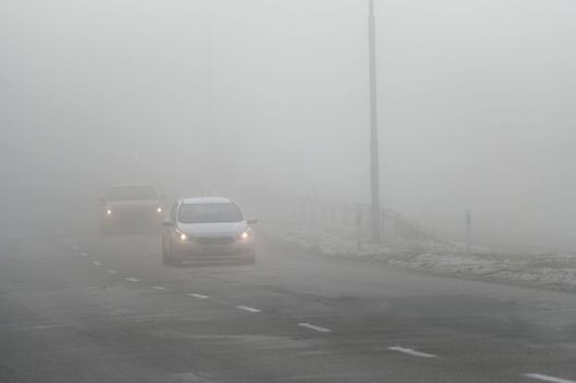 Cars in the fog. Bad winter weather and dangerous automobile traffic on the road. Light vehicles in fog.
